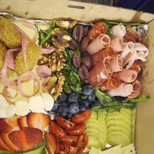 Overhead view of a grazing box with falafel, rolled cold meats, walnuts, olives, blueberries, strawberries, tomatoes and sliced cucumber