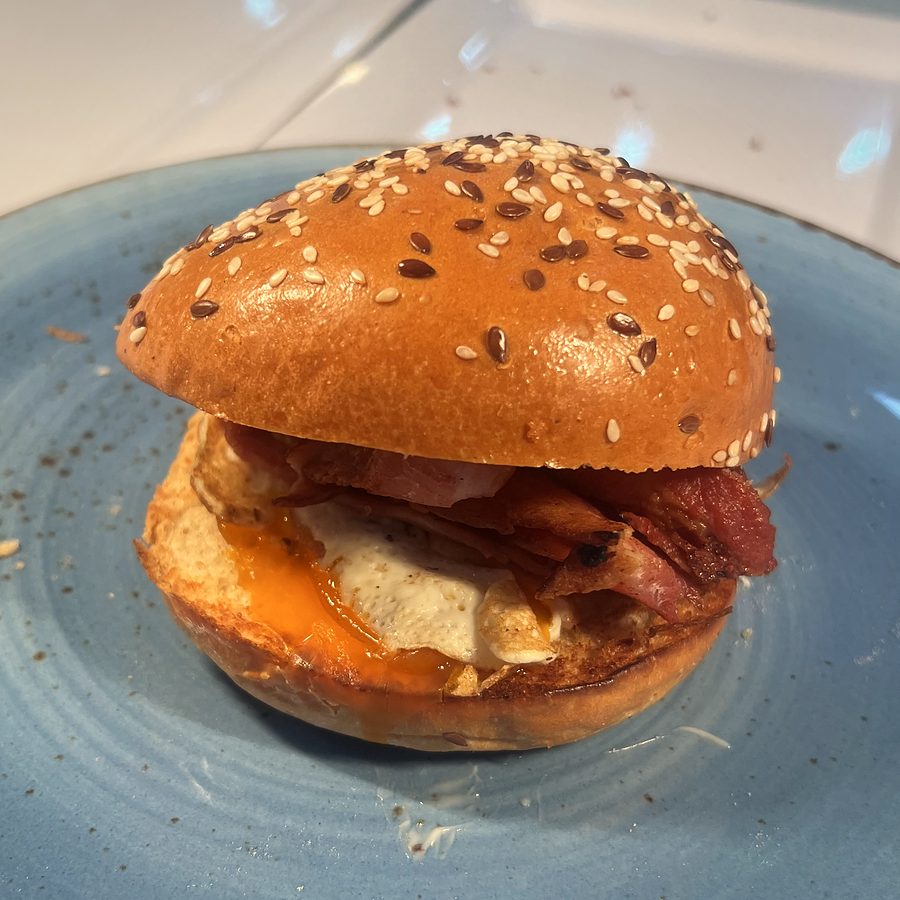 An egg and bacon roll on a sesame bun with a runny yolk, served on a blue plate