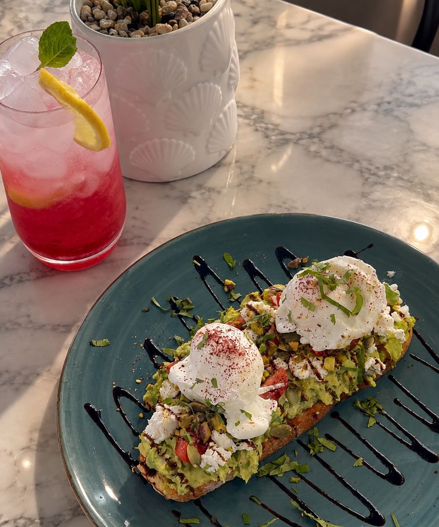 Avo toast with two poached eggs on a teal plate, beside a pink Hibiscus Lemonade with a lemon slice and mint
