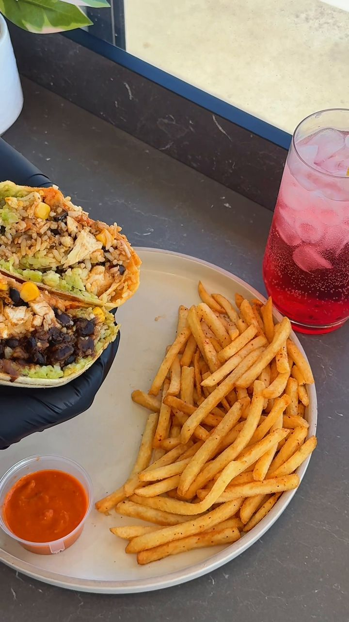 A burrito wrap cut open beside a plate of chips and a pink Hibiscus Lemonade